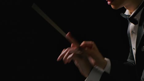 symphony orchestra conductor wearing suit is directing musicians with movement of baton, isolated on black background. conducting, directing a musical performance with visible gestures. close up