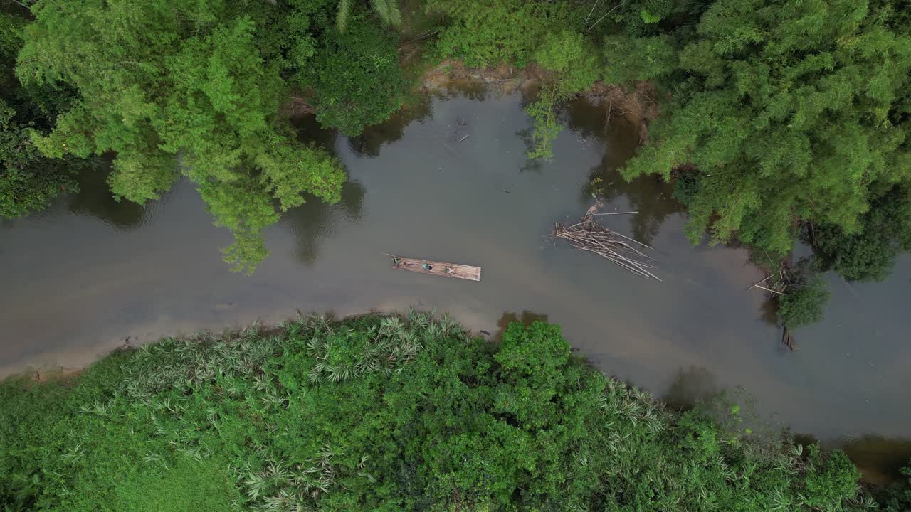 A detailed top-down aerial shot of a single traditional bamboo raft carrying tourists. The raft is being guided around a sharp bend in the Sok River, surrounded by dense, lush tropical jungle vegetati