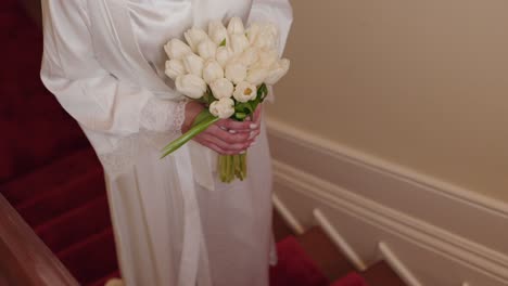 close up of bride with white tulips walking down red carpet stairs
