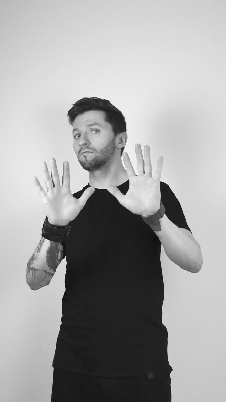 Grayscale footage of a white tattooed man lifting up his arms and starts waving his hands in front of the camera, palms out, indicating and showing he wants you to stop something, he shakes his head.