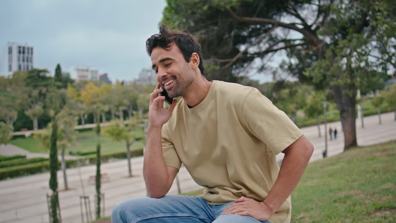행복한 남자가 전화번호를 누르며 길거리 벤치에서 긴장을 풀고, 남자가 전화를 시작합니다.