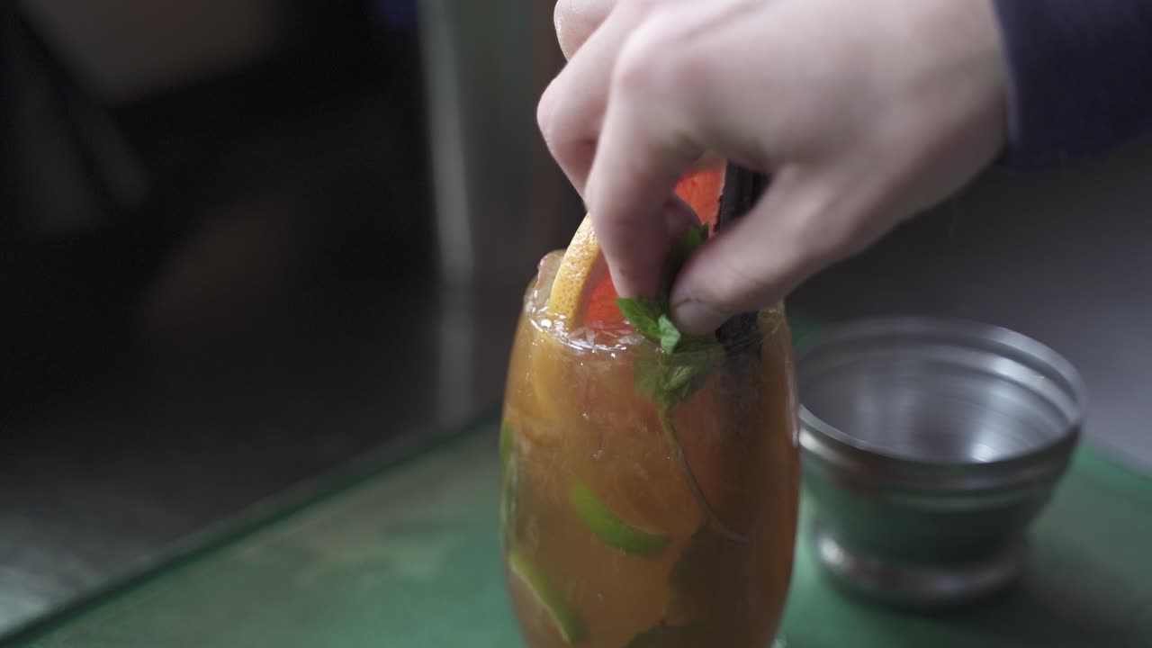 primer plano de barman agregando hoja de menta encima de bebida alcohólica de cynar en vidrio en la fiesta, cámara lenta