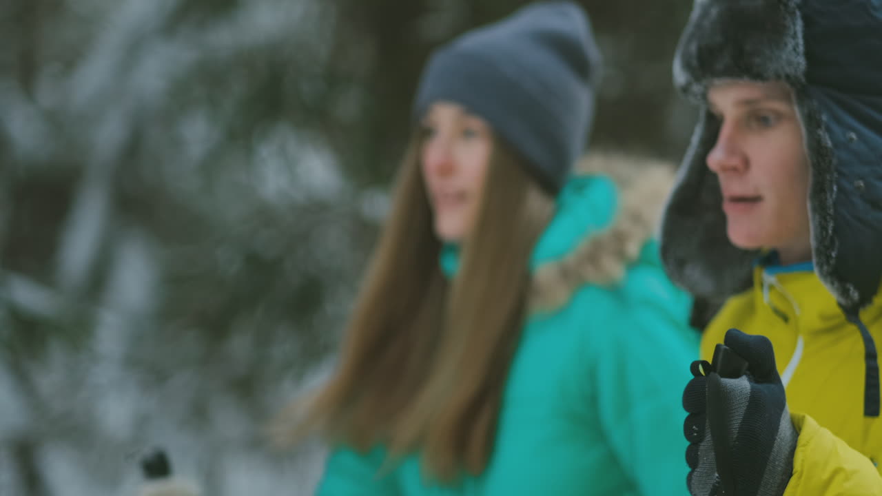 겨울 숲 속에서 노란색 재킷을 입은 남자와 파란색 점프수트를 입은 여자가 슬로우 모션으로 스키를 타고 있다