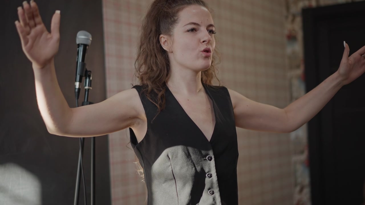 Hvit kvinne i intens audition leverer kraftfull solo under studiolys, mikrofonstativ, kontrollert pust og frasering, dramatisk ansiktsuttrykk, emosjonell projeksjon, fokus på teknikk.