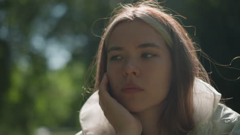 close-up of young woman in translucent raincoat pulling down hood with left hand, wearing smart watch and gazing contemplatively into distance