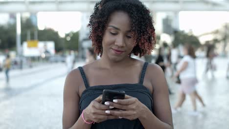 cheerful young woman texting on smartphone during stroll