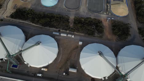 Trailer-truck-passing-through-large-silos-of-grain-processing-plant,-aerial-tracking-shot