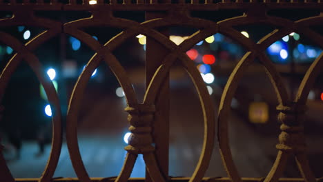 close view of a decorative iron fence with a bokeh effect of city lights and car headlights in the background at night