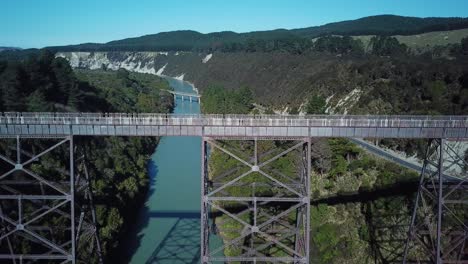 vista aérea, primer plano de un puente abandonado en nueva zelanda, sobre un río azul, deslice hacia la izquierda