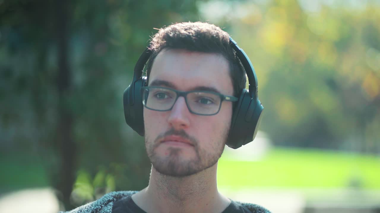 el tipo de hombre con gafas usa audífonos sentado en el parque escucha música para relajarse