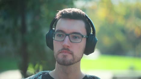 man dude glasses wears headphones sitting in park listens to music to vibe relax