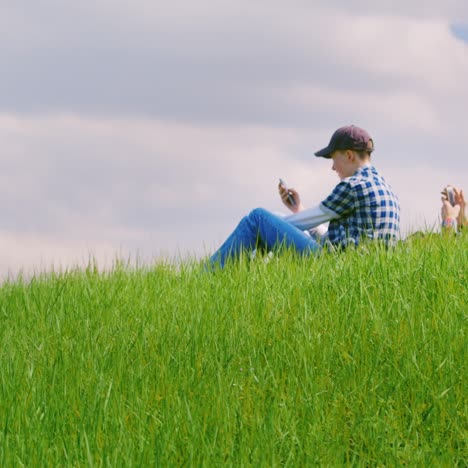 two teenage boys are sitting on a green meadow using mobile phones 2