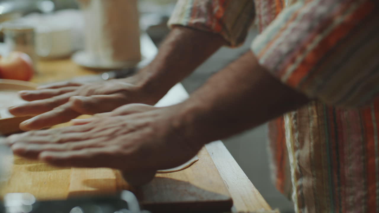 manos de un hombre rodando la masa en pan plano delgado en la mesa de la cocina de madera