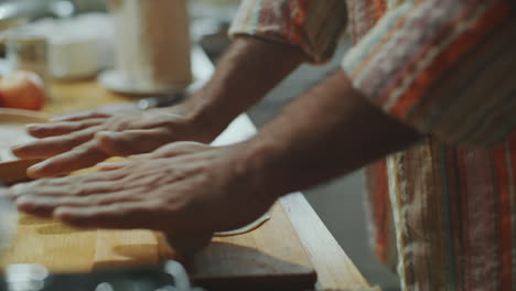 hands of man rolling dough into thin flatbread on wooden kitchen table