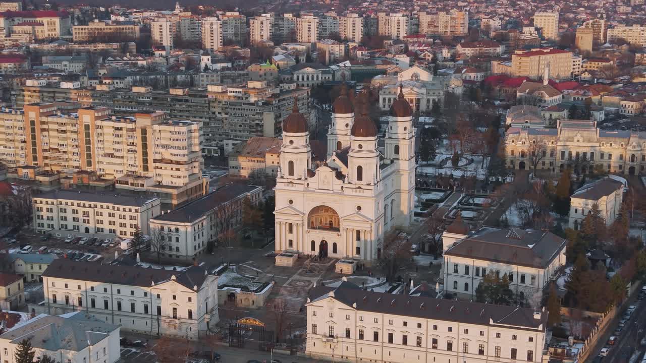 Vista aérea de drone do pôr do sol da Catedrala Mitropolitană coberta de neve em Iași, Romênia, com luz dourada nas cúpulas brancas e na paisagem urbana de inverno ao redor