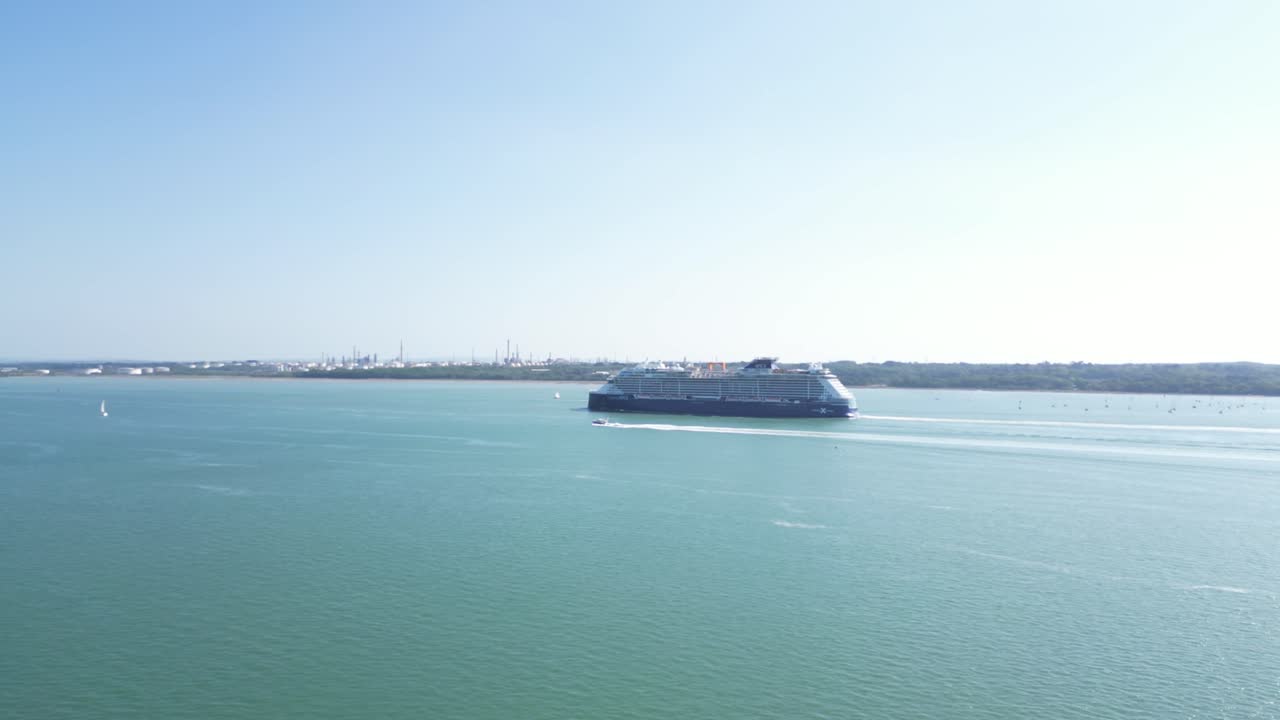 Aerial drone footage of a large cruise ship sailing through Southampton Water near Netley Abbey, Hampshire. Clear skies and calm, turquoise waters frame this tranquil maritime scene.