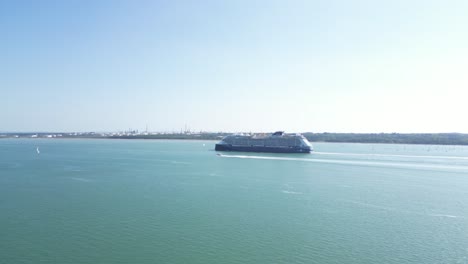 aerial drone footage of a large cruise ship sailing through southampton water near netley abbey, hampshire. clear skies and calm, turquoise waters frame this tranquil maritime scene.