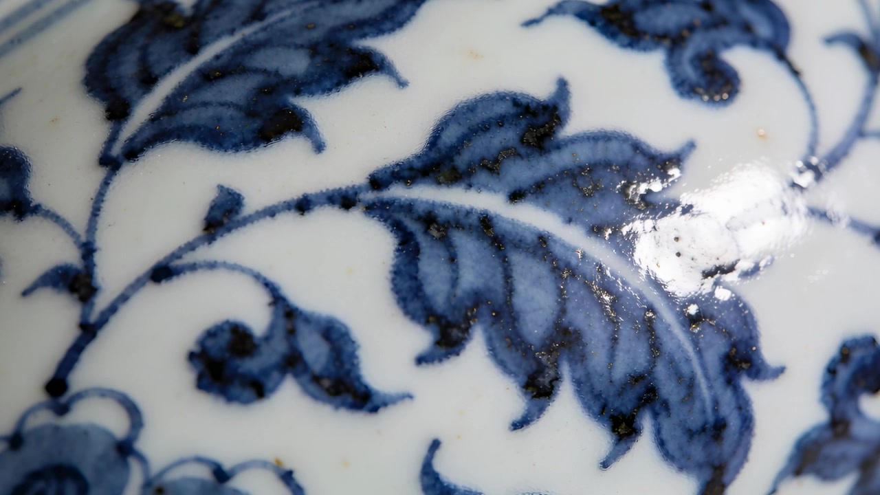 Telecamera e illuminazione che si muovono rivelando un macro di porcellana blu e bianca, ricciolo di foglia color cobalto, lucentezza, puntini di ferro