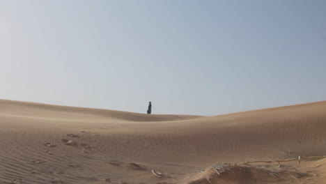 extreme long shot of a muslim woman in traditional dress and hijab walking in a windy desert