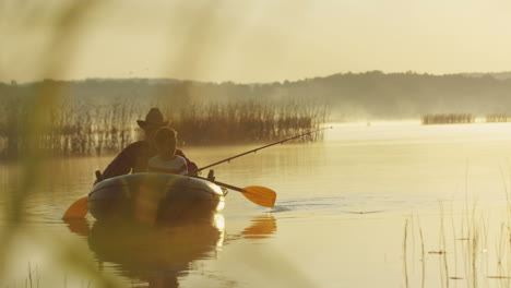 old man with a hat and his grandson on a boat fishing with a rod on the lake on a cloudy morning