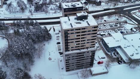 modern grey beige apartment building covered in snow next to coniferous forest, drone