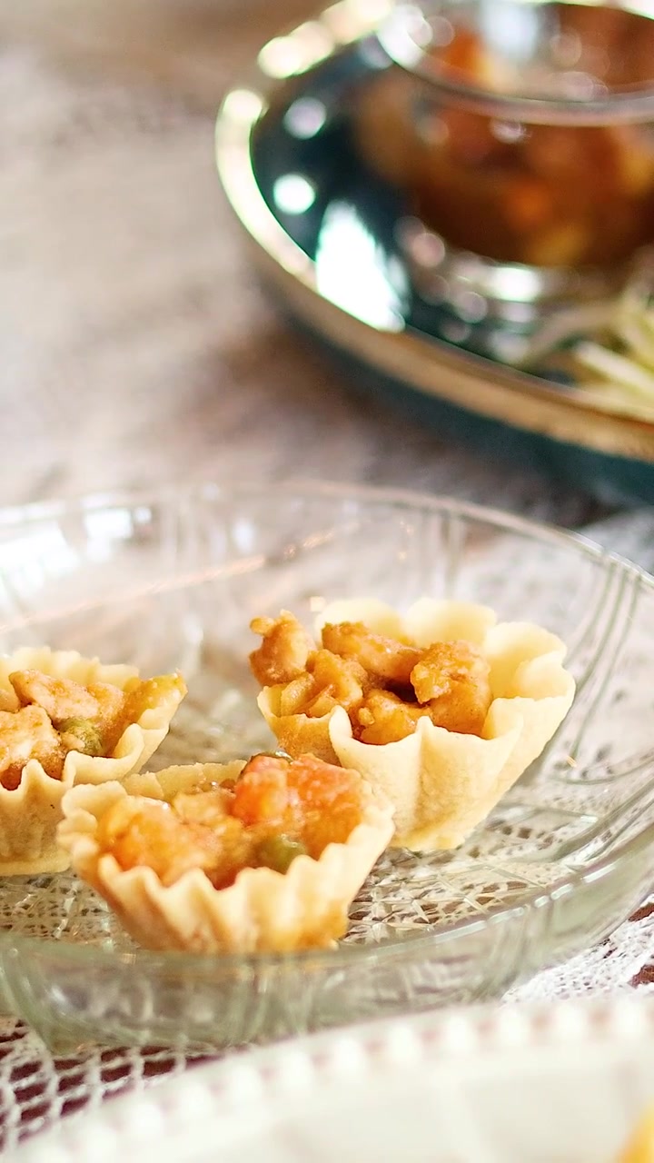 Un primo piano verticale mostra mani che prendono tortine salate tradizionali thailandesi da un piatto di vetro.