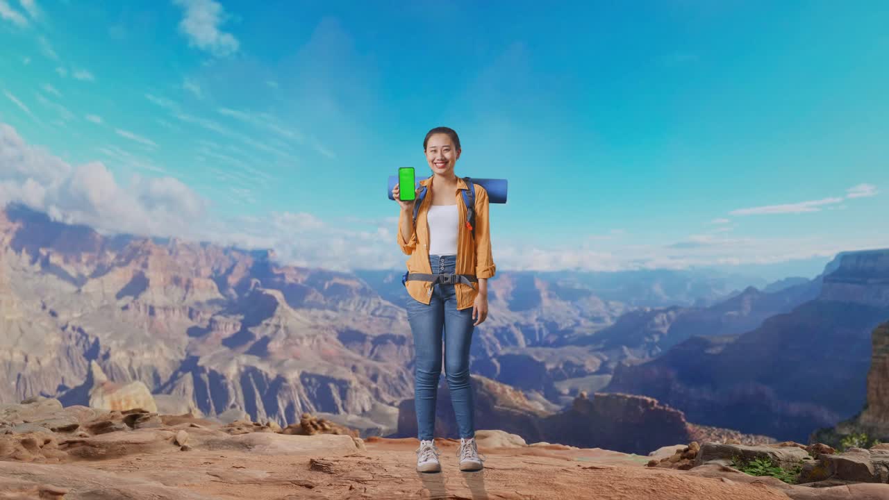 Full Body Of Asian Female Hiker With Mountaineering Backpack Smiling And Showing Mock Up Green Screen Smartphone While Traveling At The Top Of Mountain