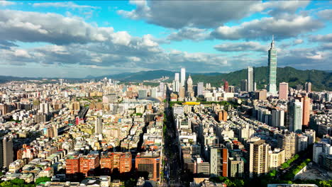 Vuelo-Aéreo-Hacia-Adelante-Sobre-La-Hermosa-Ciudad-Brillante-De-Taipei-Durante-El-Día-Nublado-Y-Soleado,-Taiwán---Vista-Panorámica-Que-Muestra-Edificios-Rascacielos-Y-Torre-101-Con-Montañas-En-El-Fondo