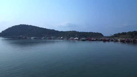 bang bao pier floating village in koh chang island, thailand, showing colorful houses and boats sailing in turquoise water. dramatic aerial view flight fly push forward drone