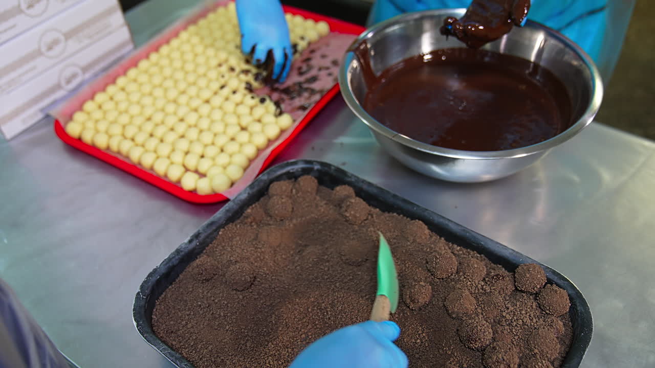 White creamy balls are thrown into the chocolate, cocoa and nuts. Chocolate truffle candies made by hands close up.