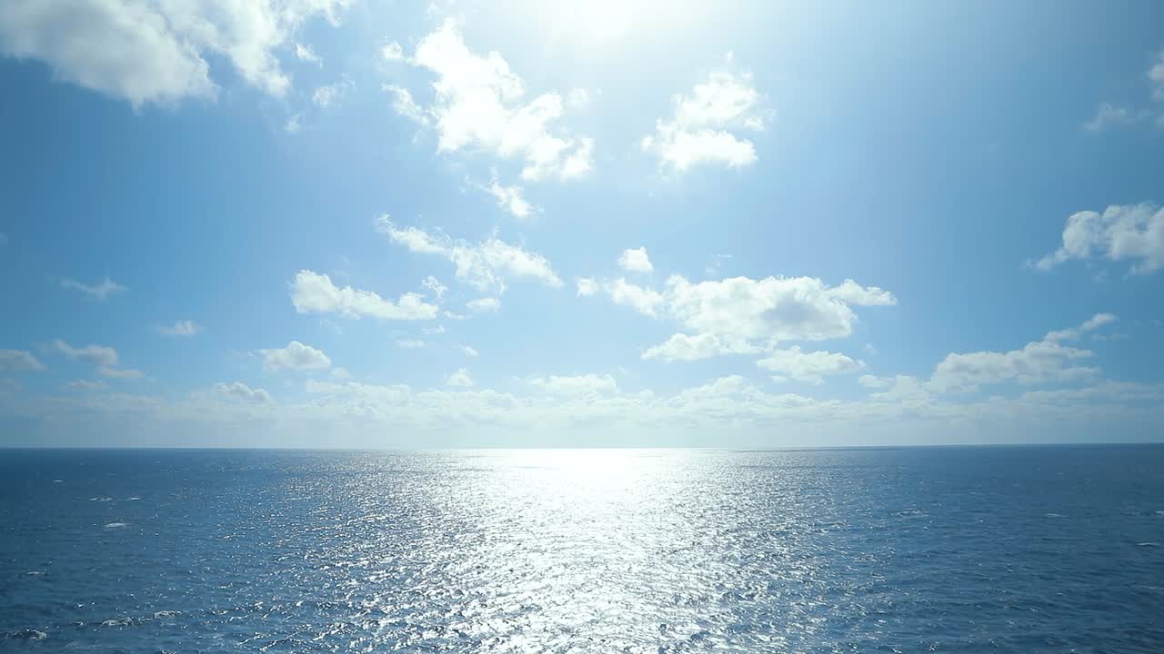 カリブ海のクルーズ船から見た大西洋の水平線に反射する太陽の光。深い青色の水面と散らばる雲が印象的です。