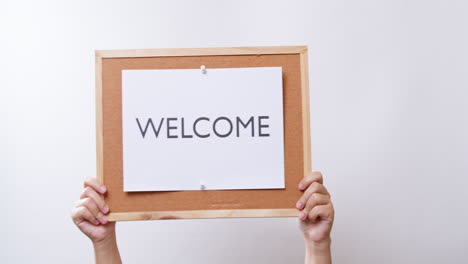 Woman's-hand-shows-the-paper-on-board-with-the-word-WELCOME-in-white-studio-background-with-copy-space