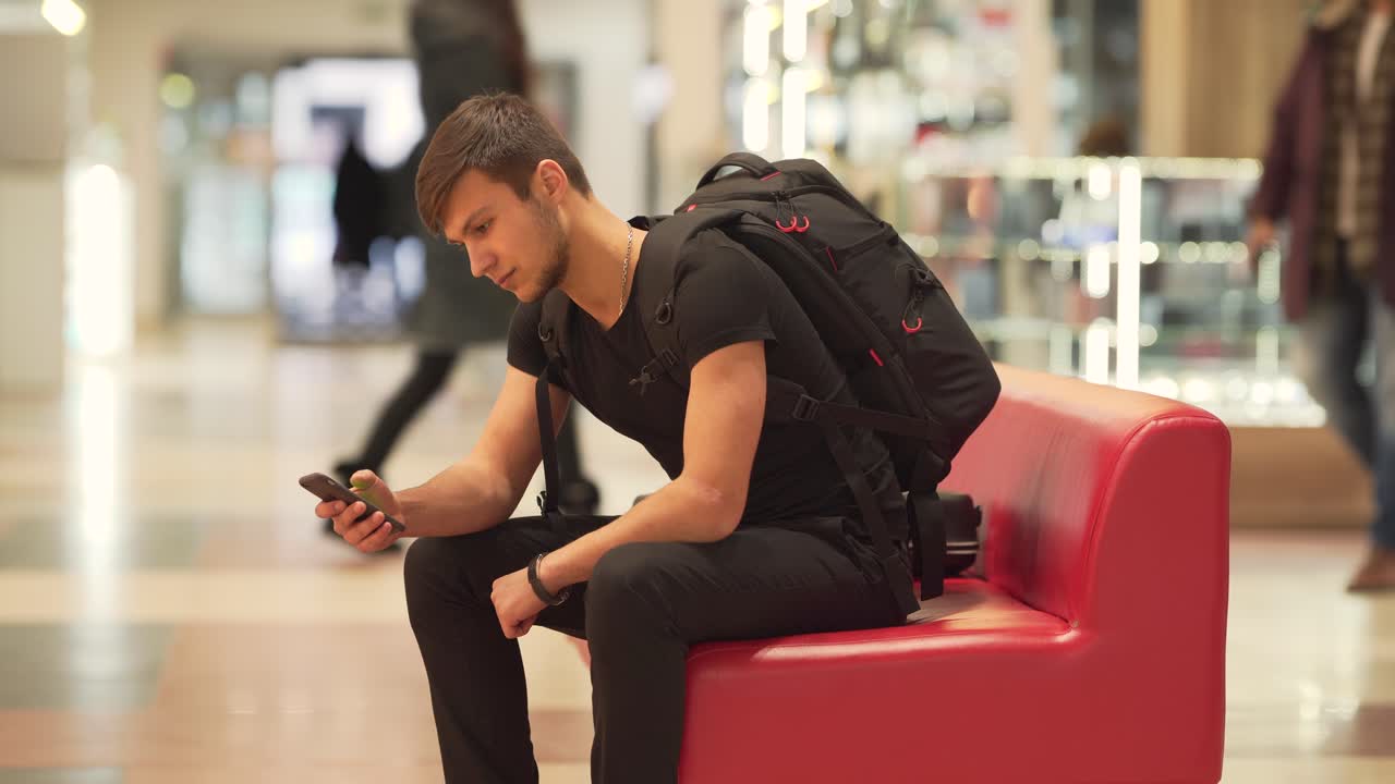un joven parado en un banco rojo sonriendo y mostrando un teléfono con llave cromática a la cámara
