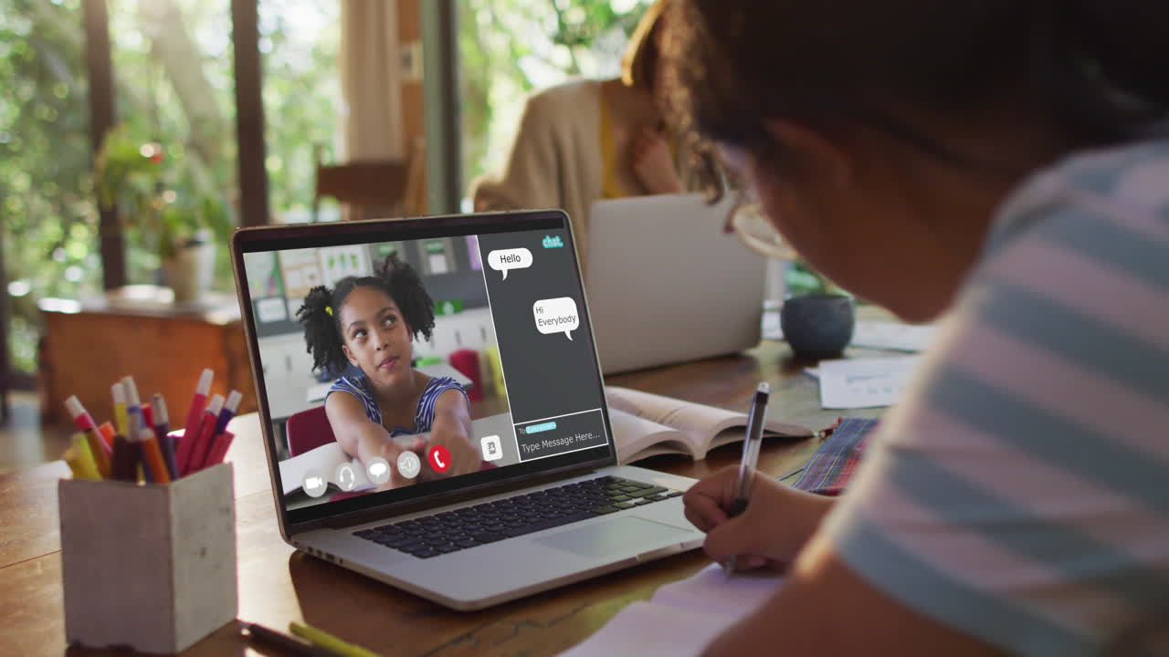 Schoolgirl using laptop for online lesson at home, with her colleague and web chat on screen