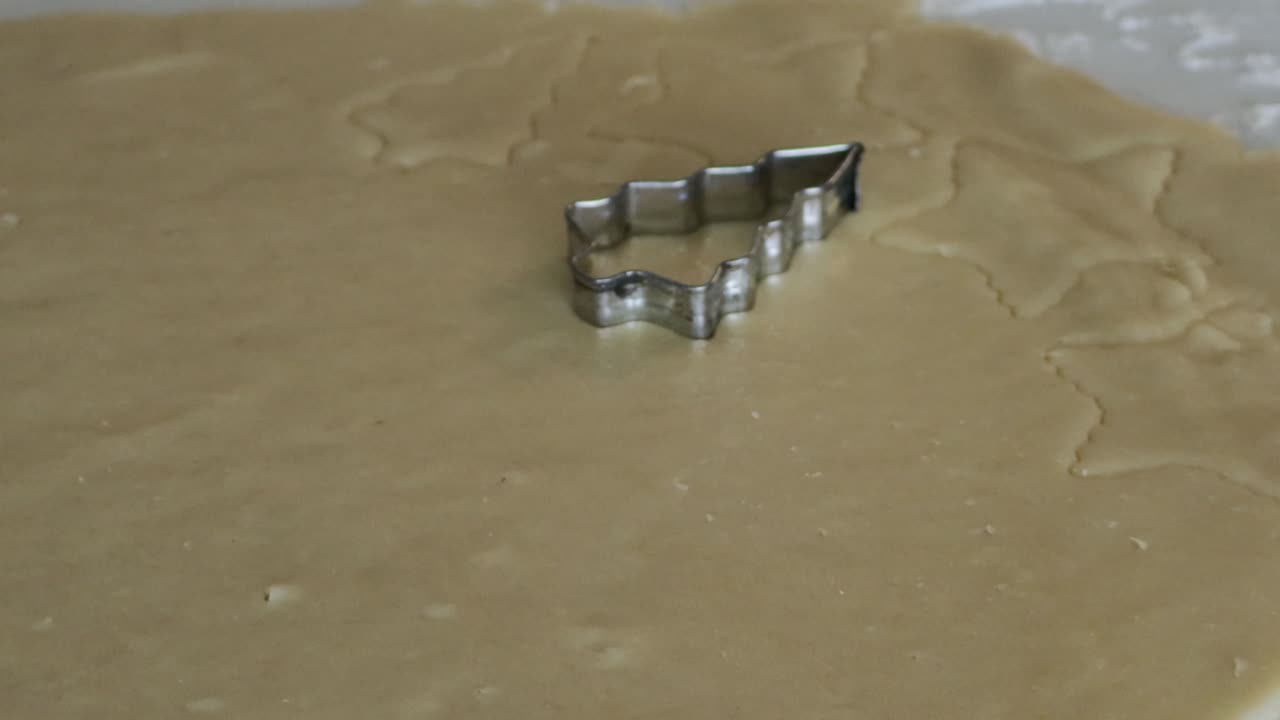 A close up shot of a Christmas tree shaped cookie cutter being used to cut out Christmas cookies from a sheet of cookie dough