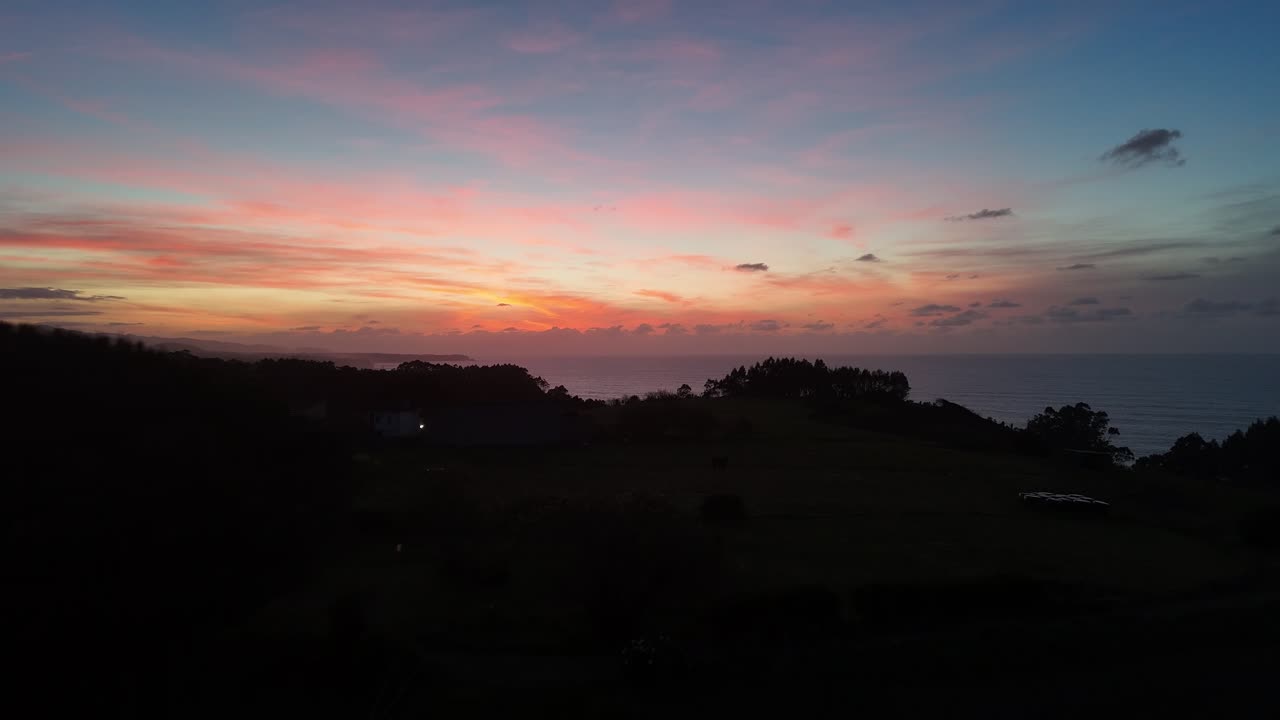 Drone view of rolling hills and sea horizon under a colorful sunset sky in Asturias Spain