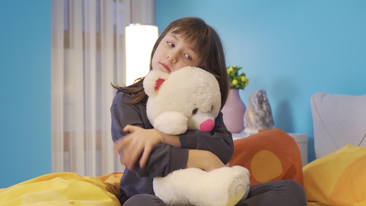 불행하고 슬픈 작은 소녀가 방에 혼자 있고 그녀의 테디 베어를 안아주고 있습니다.