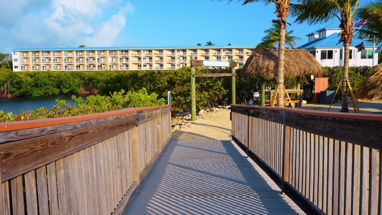 Ponte di legno per resort con marina a Key West. Una passerella in legno conduce all'area del porto turistico con palme ed edifici del resort a Key West.