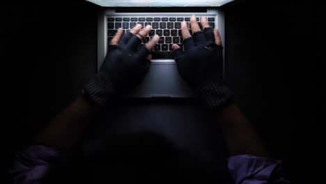 person typing on laptop with gloves at night