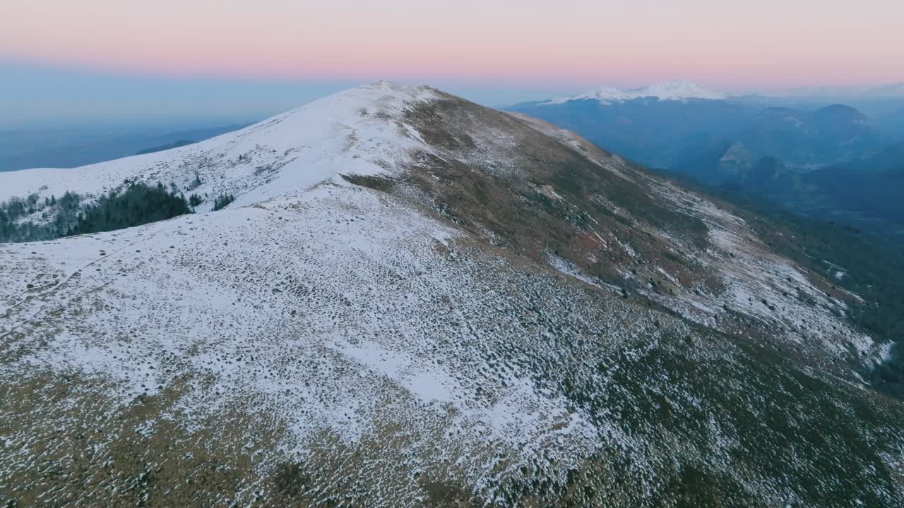 Aerial view of Pyrenees snowy mountains at sunrise, tranquil scene with pink hues.