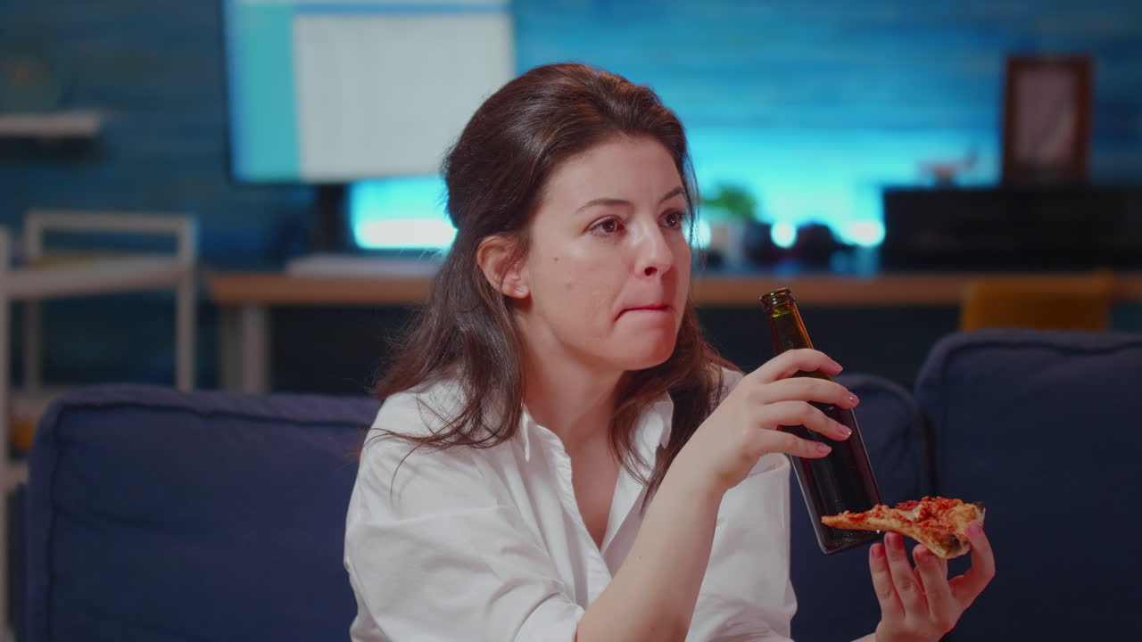Caucasian woman holding slide of pizza while drinking beer