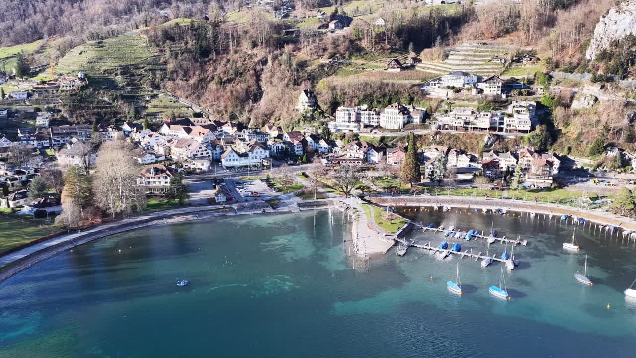 Aerial view of Weesen, Switzerland, showcasing its lakeside promenade, clear turquoise waters, hillside homes, and moored boats. Bright alpine light highlights this peaceful village setting