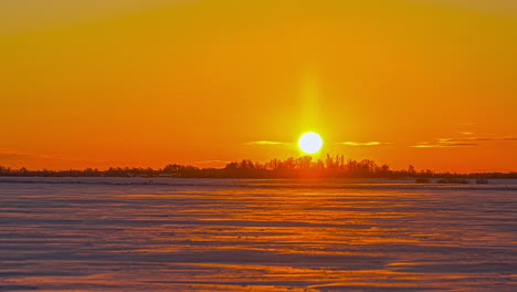 cielo naranja intenso mientras el orbe solar se pone debajo del horizonte sobre un paisaje nevado