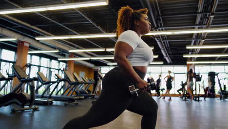 plus-size woman doing dumbbell lunges in gym