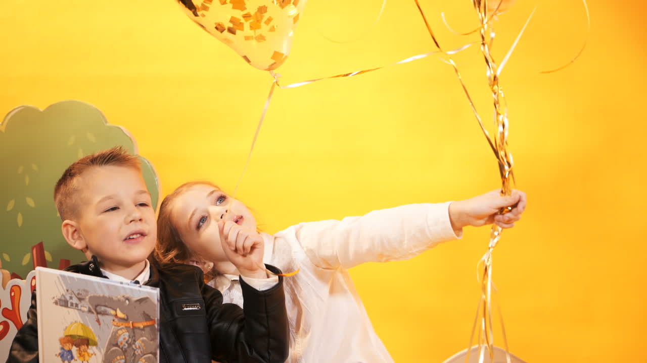 Happy children with balloons on a yellow background in the studio. Celebration and party. Having fun.