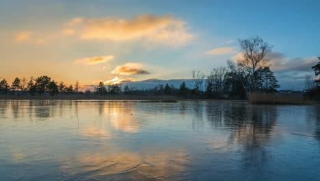 time lapse with reflection on an ice surface. it's sunset on a lake. the clouds are lit yellow on this cold winter day. the sky is blue. you can see ice crystals. the sun is setting