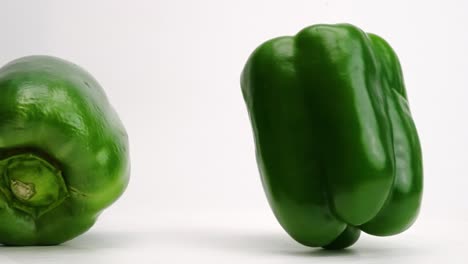 green bell peppers vegetable produce falling and bouncing and rolling around on white table top in slow motion