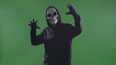 hombre aterrador en la sudadera con capucha usando máscara de halloween haciendo un gesto aterrador sobre el fondo de la pantalla verde