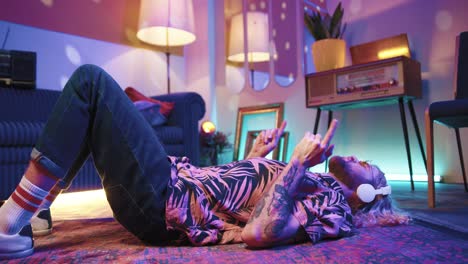 young stylish caucasian man with long hair in headphones lying on the floor and listening to music in a retro party at home