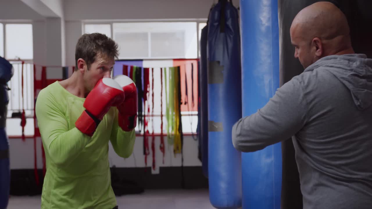Uomo caucasico che usa il sacco da boxe con un allenatore in palestra di boxe